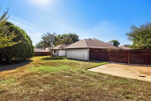 A residential property with a fenced backyard, a single-story house with a gabled roof, and a clear sky. - Spacious 4-bedroom house in enjoyable Plano (Plano)