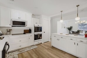 A modern kitchen with white cabinetry, a microwave, oven, and a hanging light fixture. - Spacious 4-bedroom house in enjoyable Plano (Plano)