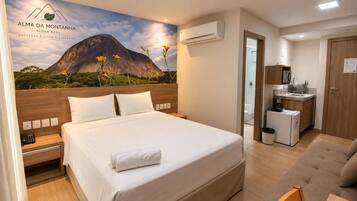 A hotel room with a bed, a sofa, a small kitchen area, and a bathroom.
