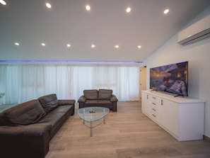 Un salon moderne avec un canapé en cuir marron, une table basse en verre et un meuble de rangement blanc intégrant un téléviseur à écran plat.