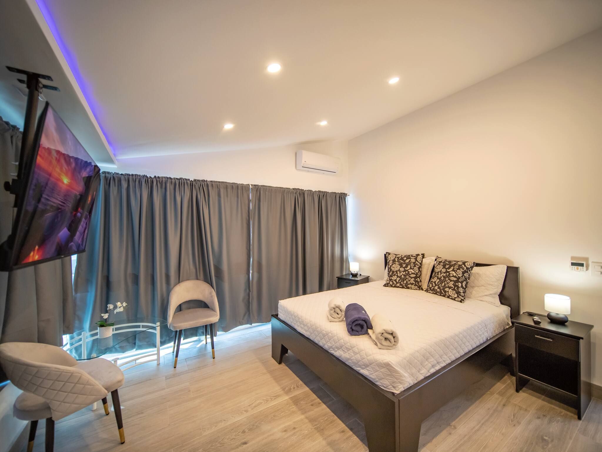 Habitación de hotel moderna con una cama grande, una silla, un televisor y un equipo de aire acondicionado.