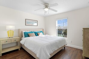 Quarto com cama, mesa de cabeceira, luminária e ventilador de teto.