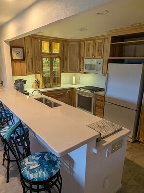 A kitchen with wooden cabinets, a white countertop, a built-in microwave, a stainless steel refrigerator, and a bar area with stools. - 2-bedroom condo in Flagstaff at Continental Country club. (Flagstaff)