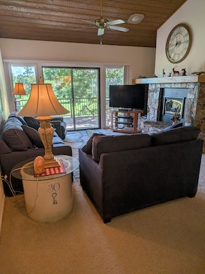 A living room with a fireplace, a television, and a large window with a view of greenery. - 2-bedroom condo in Flagstaff at Continental Country club. (Flagstaff)