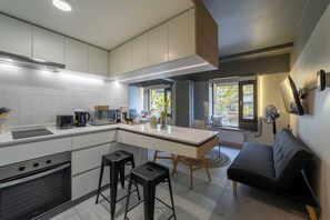 Eine moderne Küche mit Kochinsel, einem Essbereich mit einer Couch und Stühlen sowie einem großen Fenster mit Blick ins Freie.