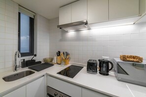 Eine moderne Küche mit weißen Schränken, einer Edelstahl-Spüle, einem Toaster, einem Wasserkocher und einer Mikrowelle.