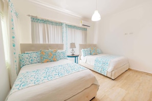 A hotel room with two beds, a bedside table with a lamp, and a window with curtains.