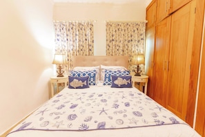 Um quarto com cama, cortinas, mesas de cabeceira e um guarda-roupa.