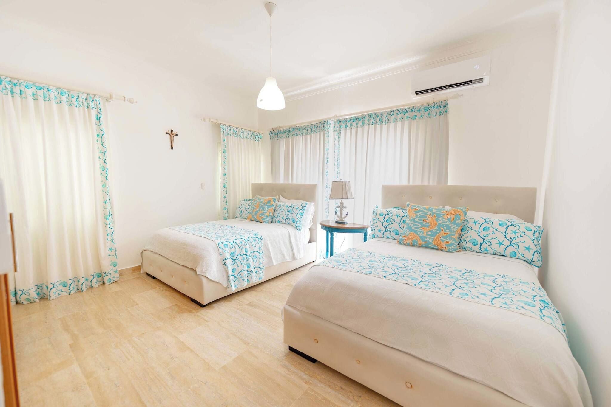 Habitación de hotel con dos camas, una mesita, una lámpara y una cruz en la pared.