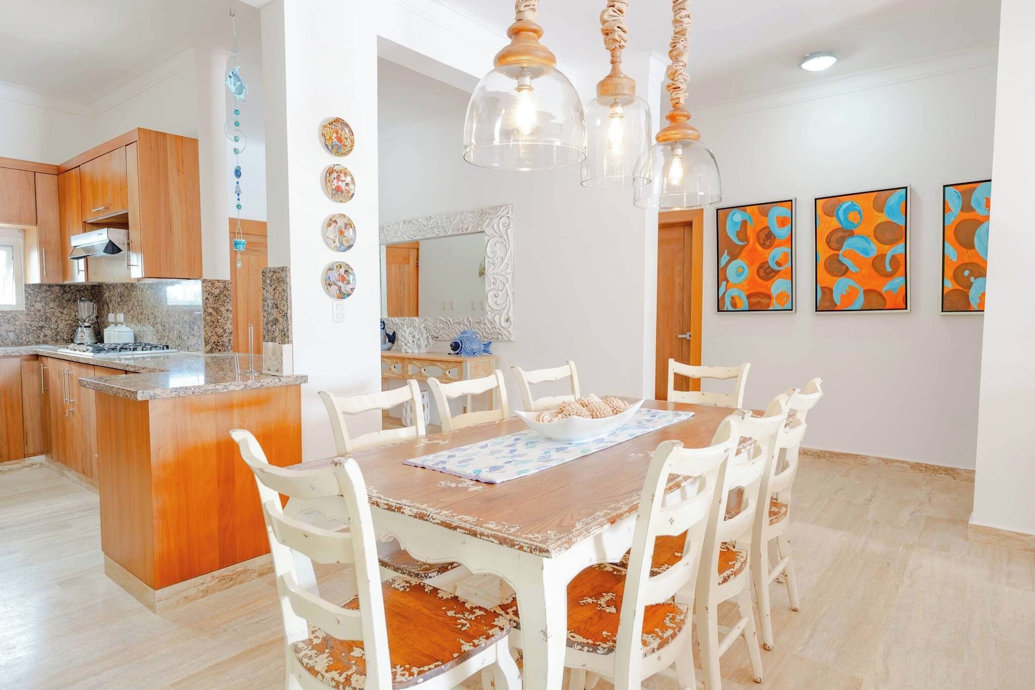 Un comedor con una mesa de madera y sillas blancas, una cocina con armarios de madera y un espejo decorativo.