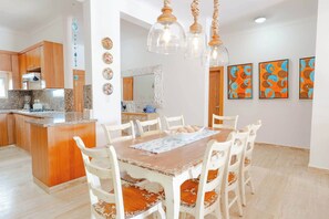 A dining area with a wooden table and white chairs, a kitchen with wooden cabinets, and a decorative mirror.