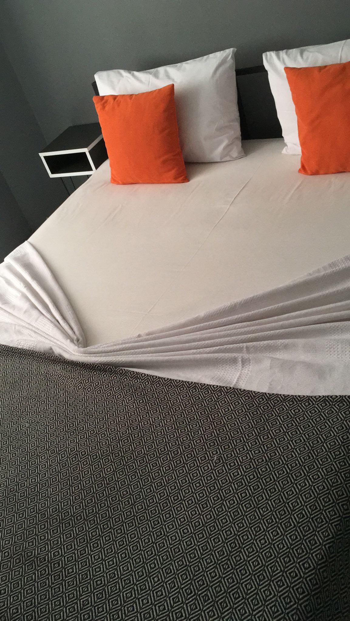 Una cama con almohadas blancas y anaranjadas, un edredón estampado y una alfombra geométrica.