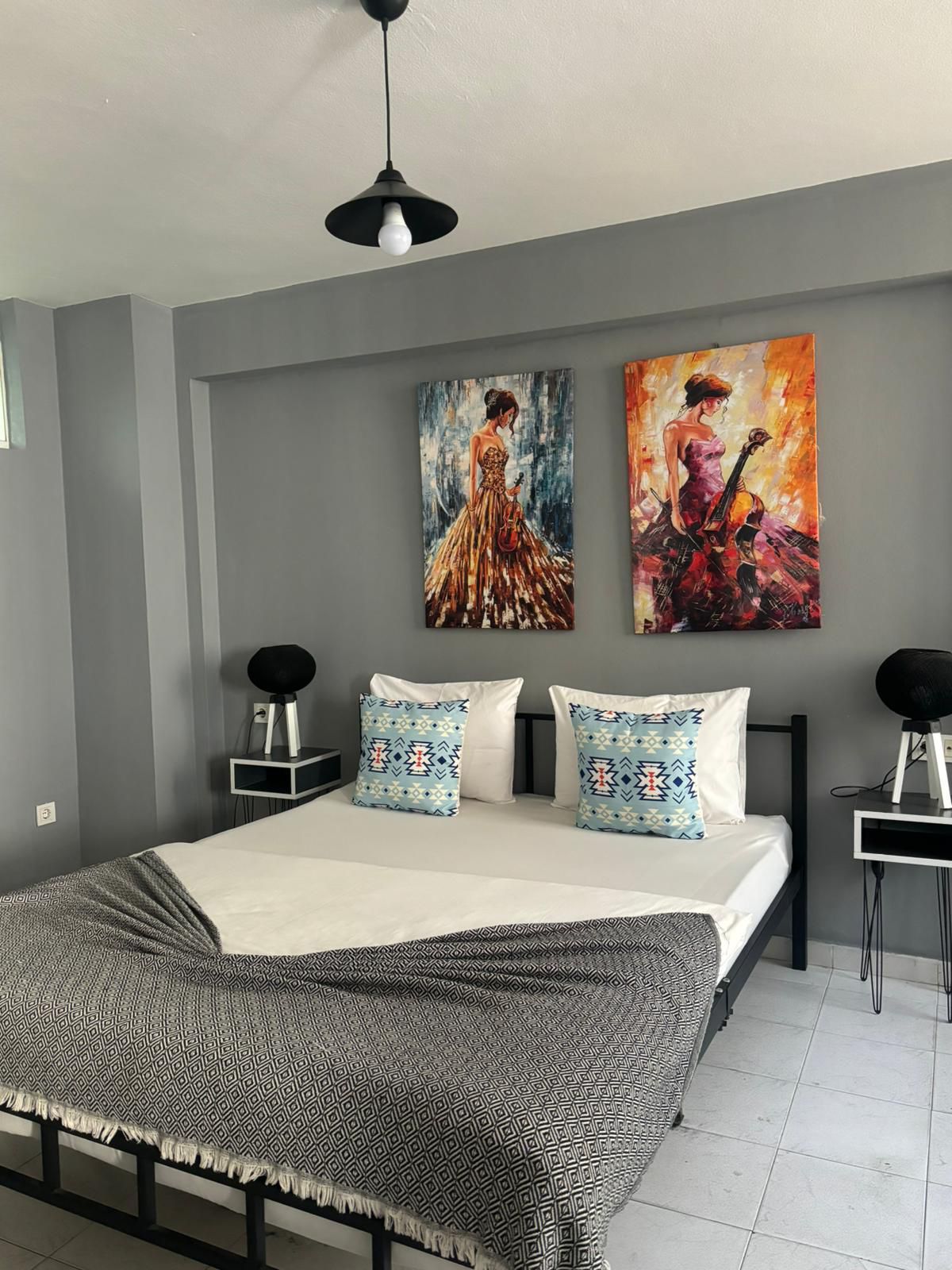 Un dormitorio moderno con una cama grande, dos mesitas de noche, una lámpara de techo negra y dos cuadros en la pared.