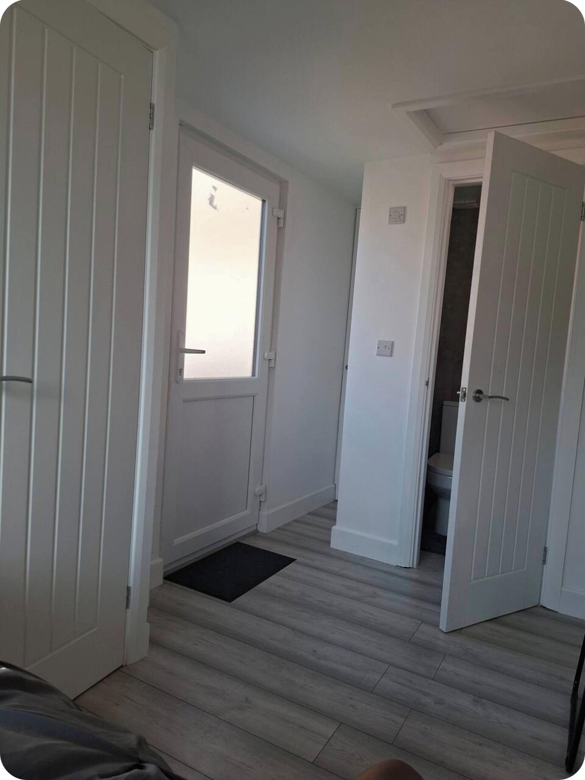 A hallway with white doors, a black doormat, and a light-colored wooden floor.