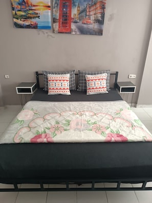 Una cama con colcha estampada de flores, dos almohadas con un diseño geométrico y un cuadro de un paisaje urbano sobre ella.