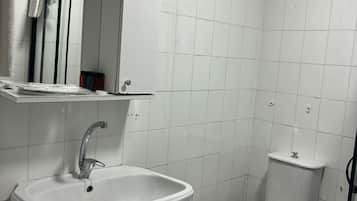 Un baño con lavamanos blanco, inodoro y espejo sobre el lavamanos.