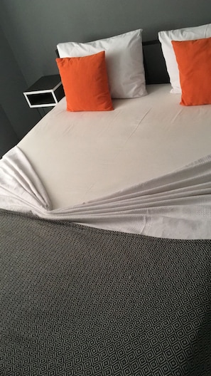 Una cama con almohadas blancas y anaranjadas, un edredón estampado y una alfombra geométrica.