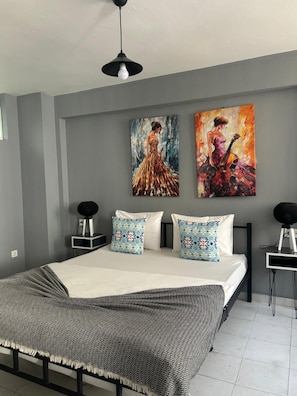 Un dormitorio moderno con una cama grande, dos mesitas de noche, una lámpara de techo negra y dos cuadros en la pared.