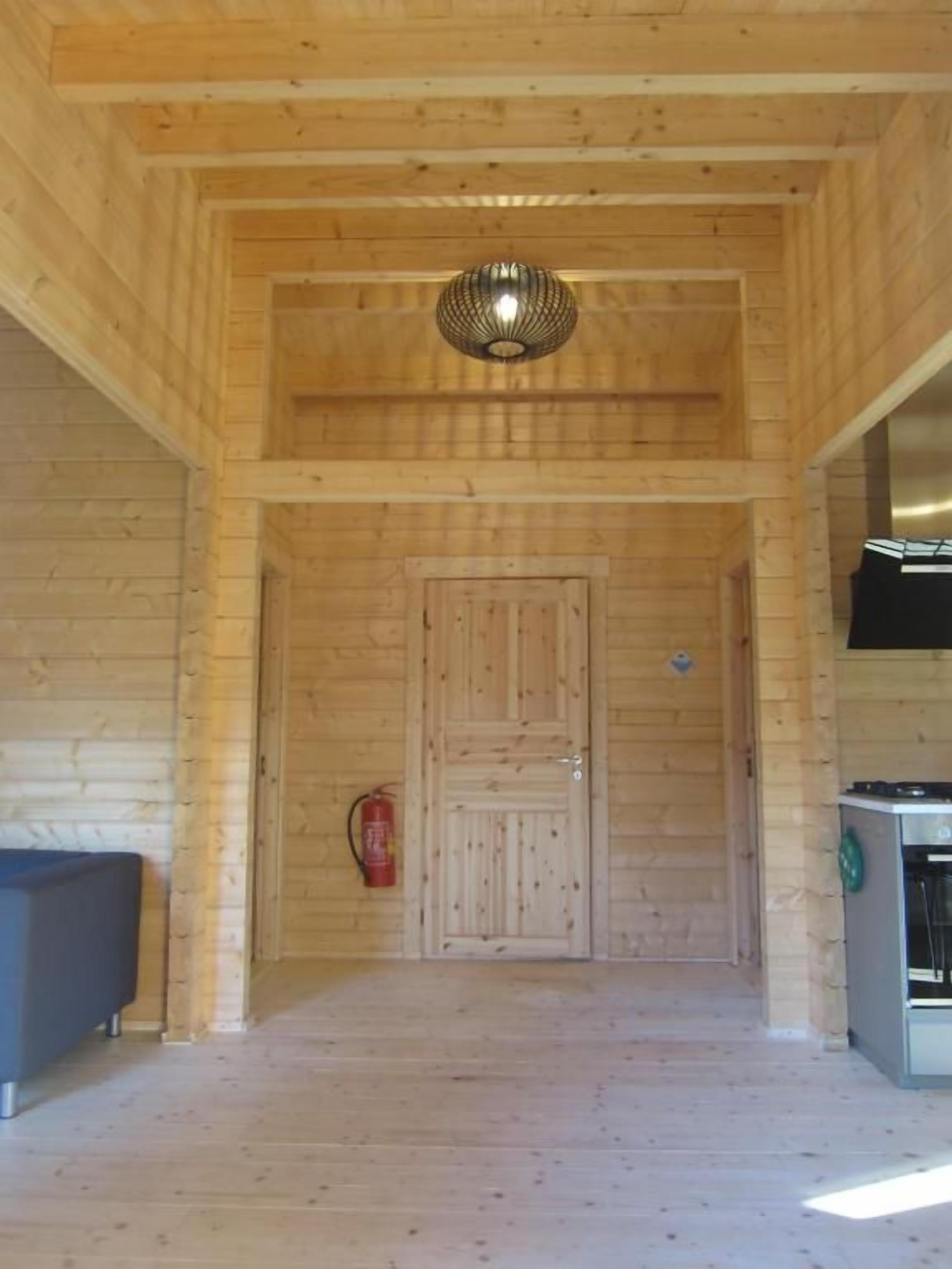 A wooden interior with a door, a fire extinguisher, and a stove.