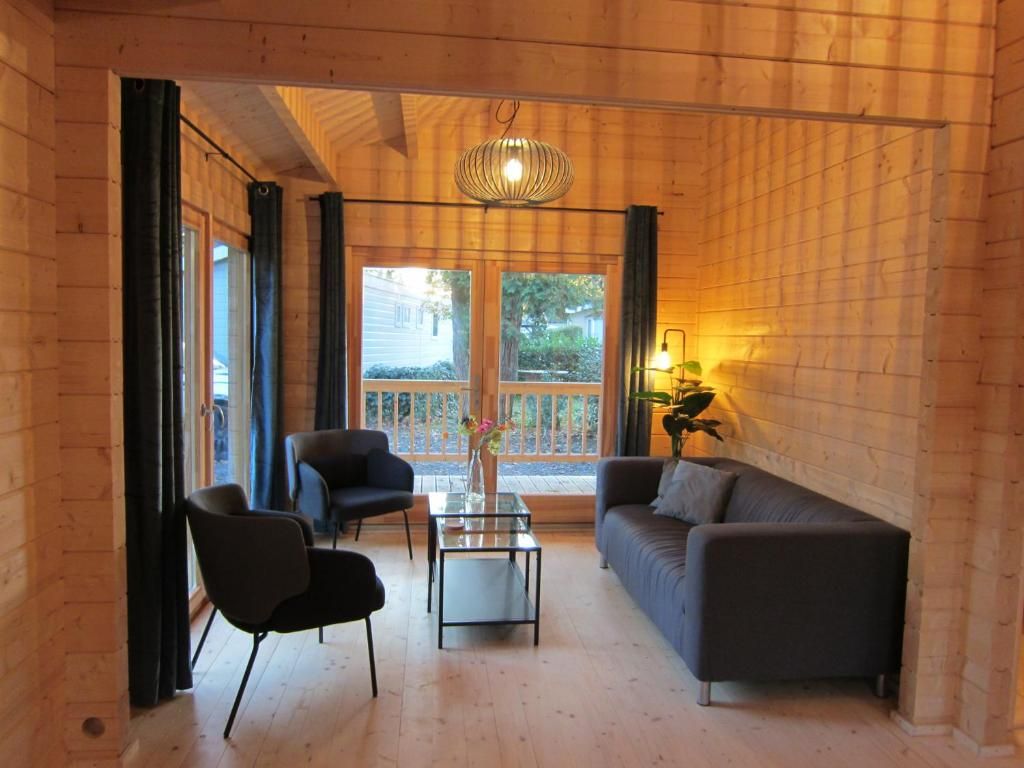 A wooden interior with a sofa, two chairs, a glass coffee table, and a hanging light fixture.