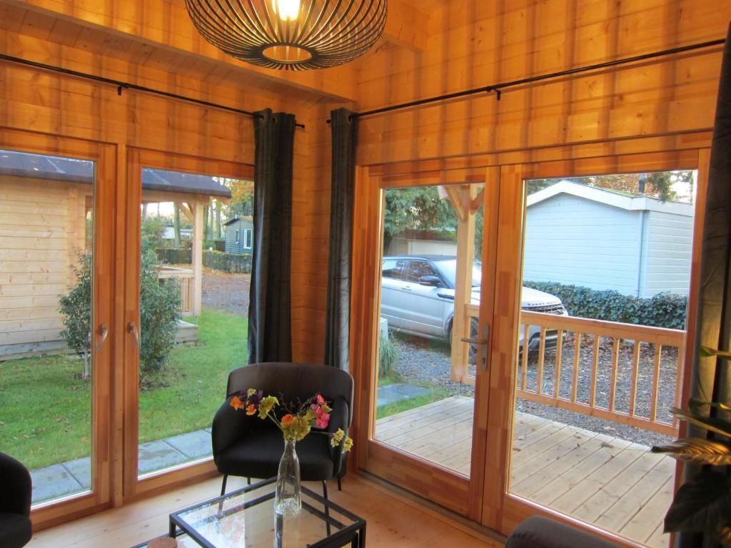 Una habitación con ventanas amplias, una mesa de vidrio y una silla con un florero.