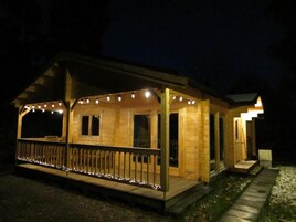 A wooden cabin with a porch, string lights, and a stone pathway.