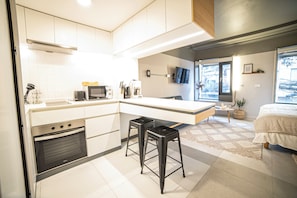 A compact kitchen with modern appliances, a dining area, and a bedroom with a large window. - Bright Studio · Selected Design (H11) (Providencia)