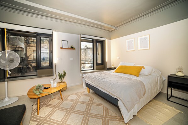 A modern bedroom with a bed, bedside tables, a desk, and a large window. - Bright Studio · Selected Design (H11) (Providencia)