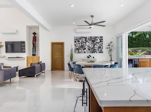 A modern kitchen with a marble countertop, a dining area with blue chairs, and a large window overlooking a garden. - Luxury Boss Villa in Sosua Hispaniola (Sosúa)