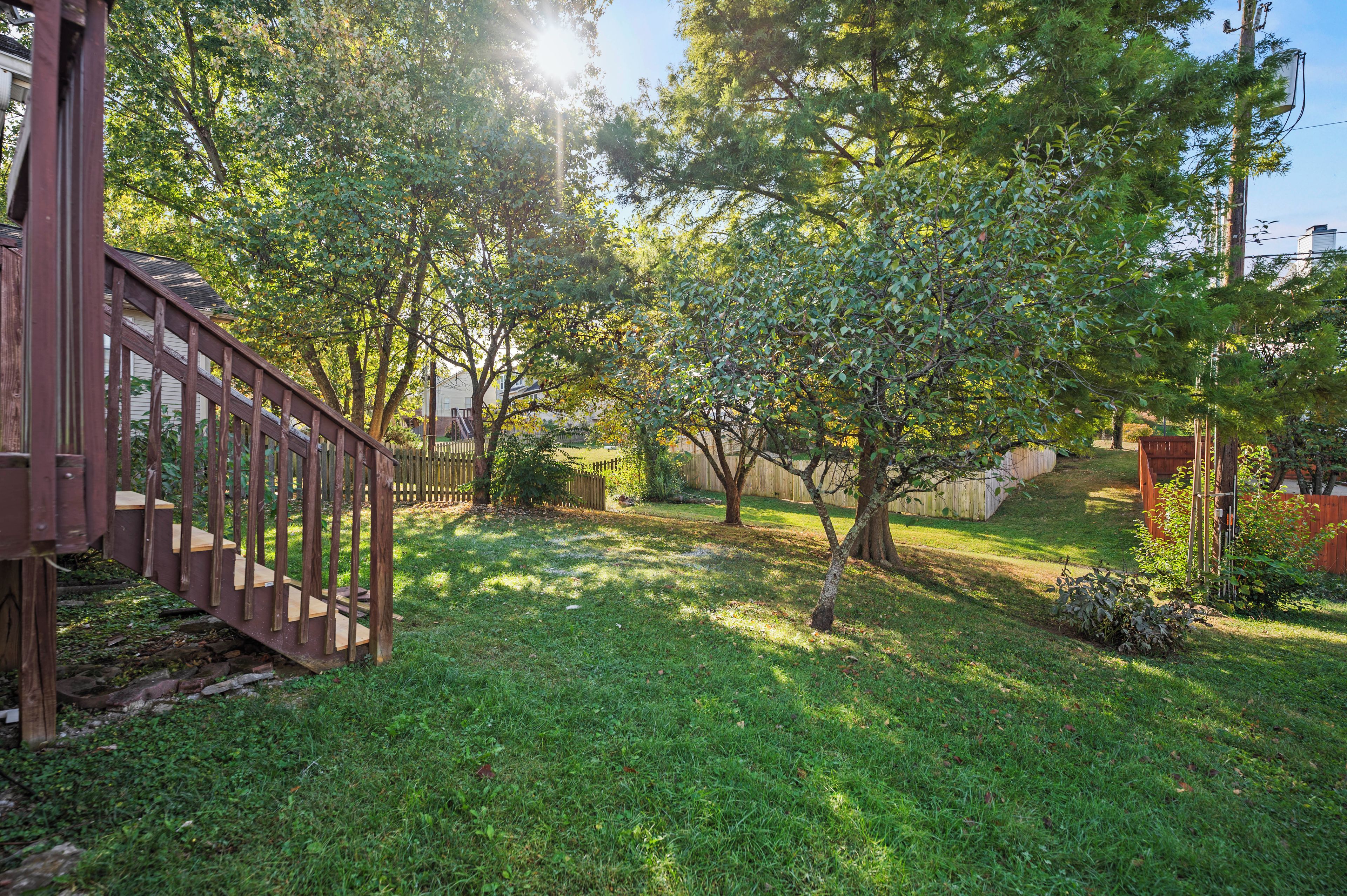 Ein Garten mit einer Holzterrasse, einem Rasen und Bäumen.