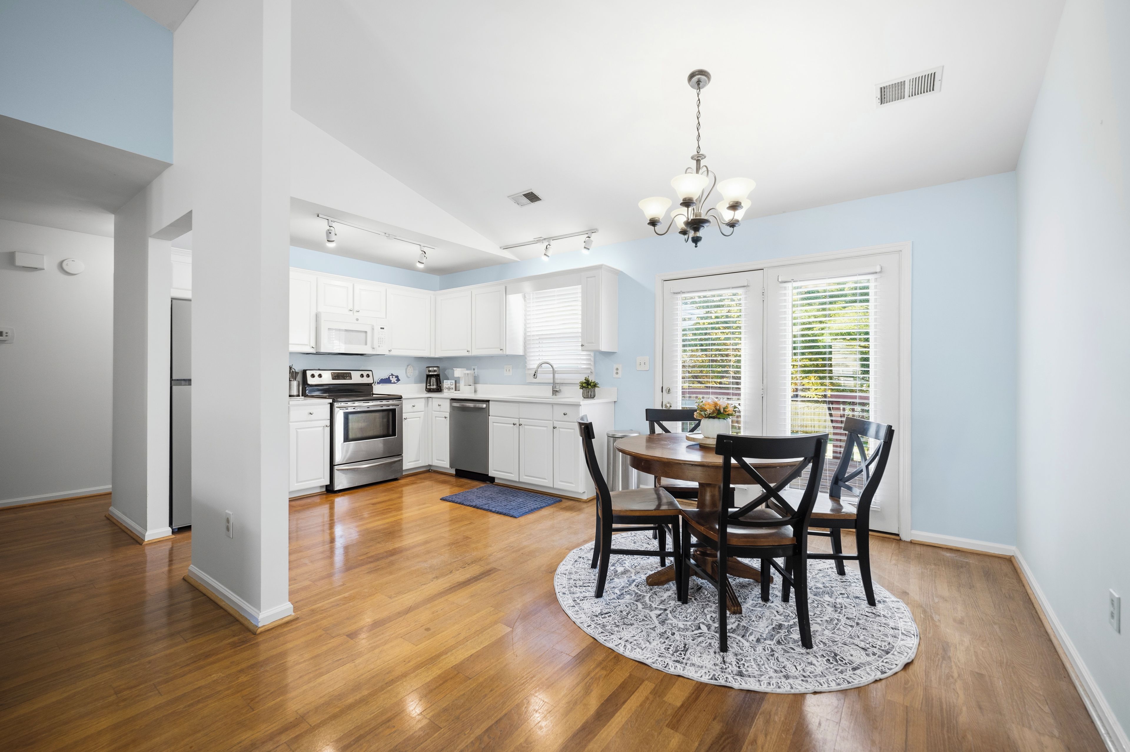 A modern kitchen with white cabinets, stainless steel appliances, and a dining area with a round table and chairs.