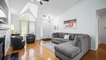 Un salón amplio con un sofá seccional gris, un sillón de cuero negro y suelo de madera.