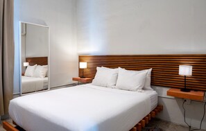 Een hotelkamer met een groot bed, een houten hoofdbord, nachtkastjes met lampen en een spiegel.