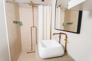 Een badkamer met een wit wastafelmeubel, een douche met glazen deur en zichtbare leidingen.