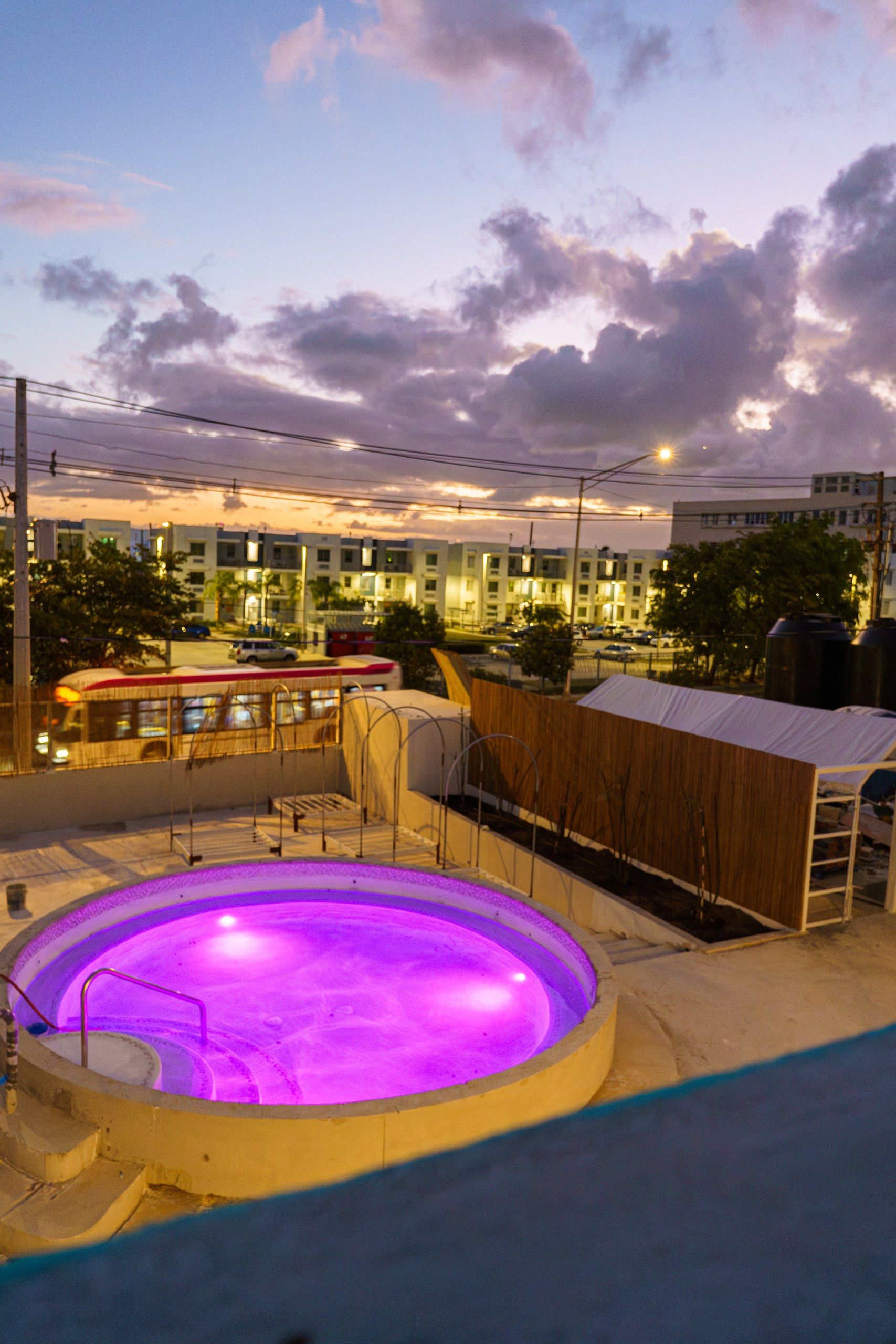 A swimming pool with a purple light, surrounded by a wooden deck and a metal fence.