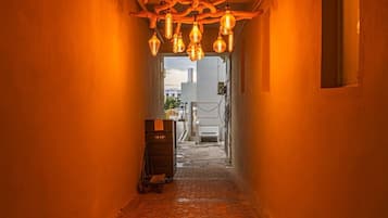 A corridor with a brick floor, wooden ceiling beams, and hanging light fixtures.