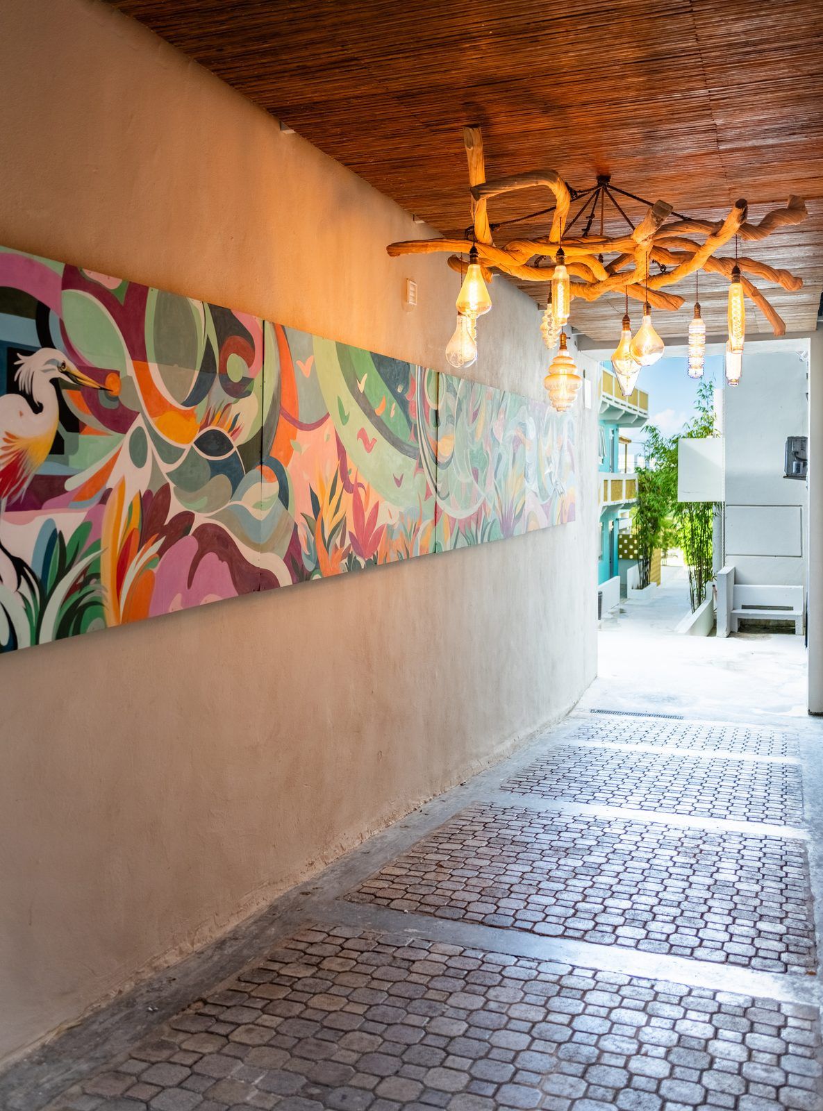 A corridor with a colorful mural, a wooden ceiling, and hanging light fixtures.