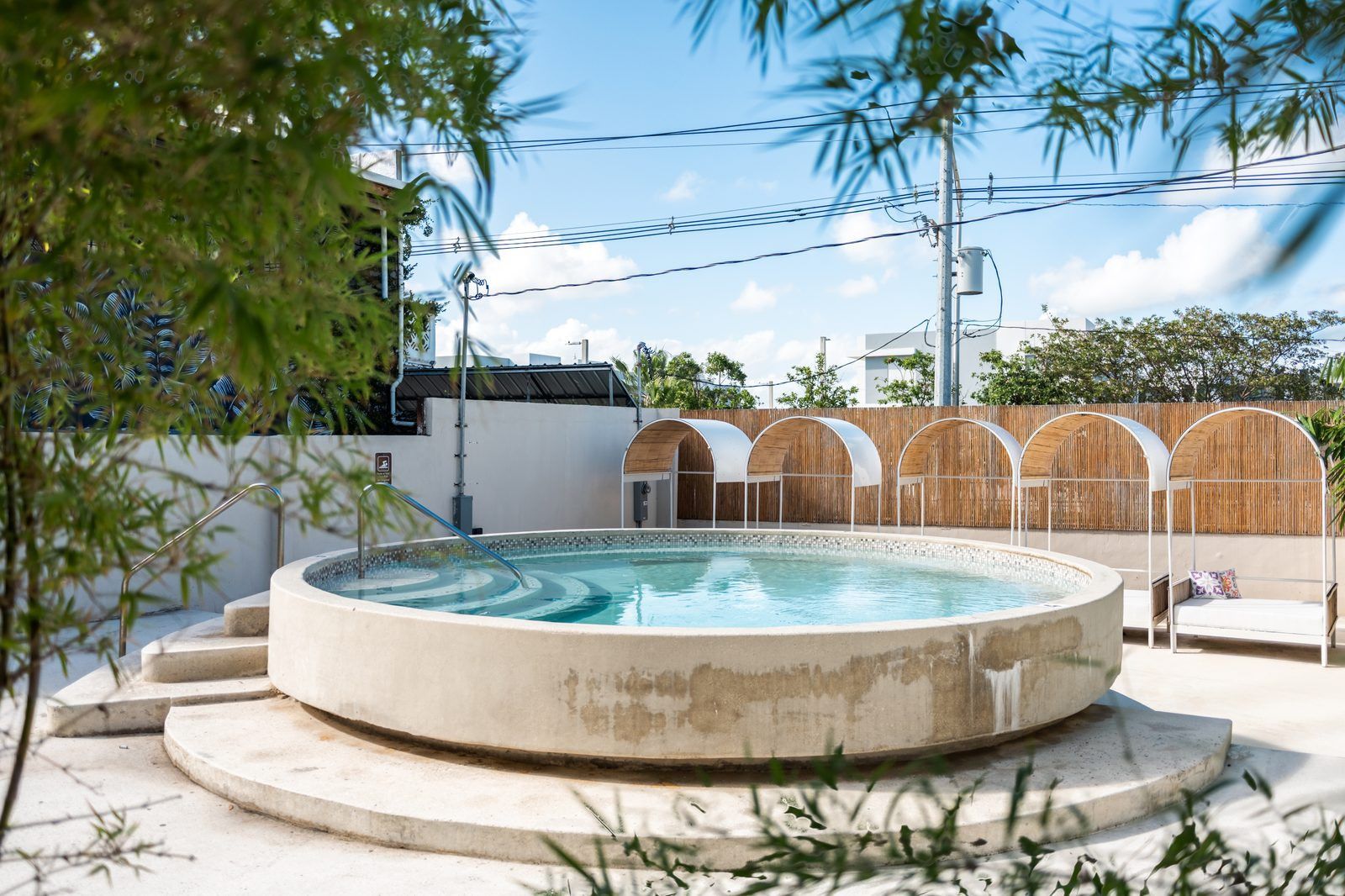 A hot tub with a wooden fence and a covered seating area in a sunny outdoor setting.