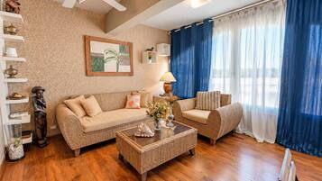 Una sala de estar con sofá, sillón, mesa de centro, piso de madera y ventilador de techo.