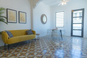 Quarto com sofá amarelo, mesa de jantar com cadeiras, espelho e porta com janela.