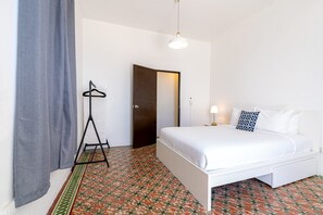 Ein Schlafzimmer mit einem Bett, einer Hängelampe, einem Kleiderständer und einem gemusterten Boden.