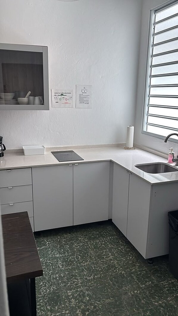 A compact kitchen with a built-in stove, a sink, and a window with blinds.