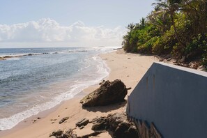 Una playa con una barrera de hormigón, costa rocosa y densa vegetación tropical.