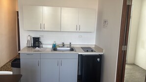 Eine kleine Küchenzeile mit Spüle, Kaffeemaschine, einem kleinen Kühlschrank und Schränken.