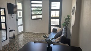 Ein Zimmer mit einer Couch, einem kleinen Tisch und einem an der Wand befestigten Fernseher.
