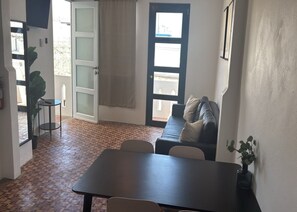 Een kamer met een eettafel, een bank, een potplant en een deur naar een buitenruimte.