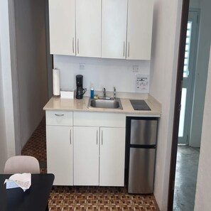 Een kleine keuken met een spoelbak, koffiezetapparaat en een koelkastje.