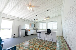 Una cocina amplia con paredes de ladrillo blanco, un refrigerador grande y una zona de comedor con dos taburetes de bar.