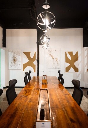 Un salón de conferencias con una larga mesa de madera, sillas negras y arte abstracto en la pared.