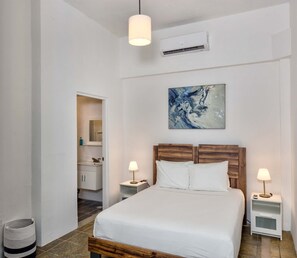 Ein Schlafzimmer mit einem Bett, Nachttischlampen, einem Gemälde und einer Klimaanlage.